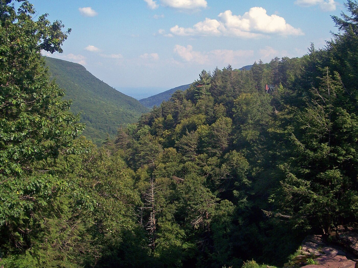 Kaaterskill Clove seen from a rock ledge on its rim, a deep forested valley opening east between two ridges toward the hazy Hudson Valley