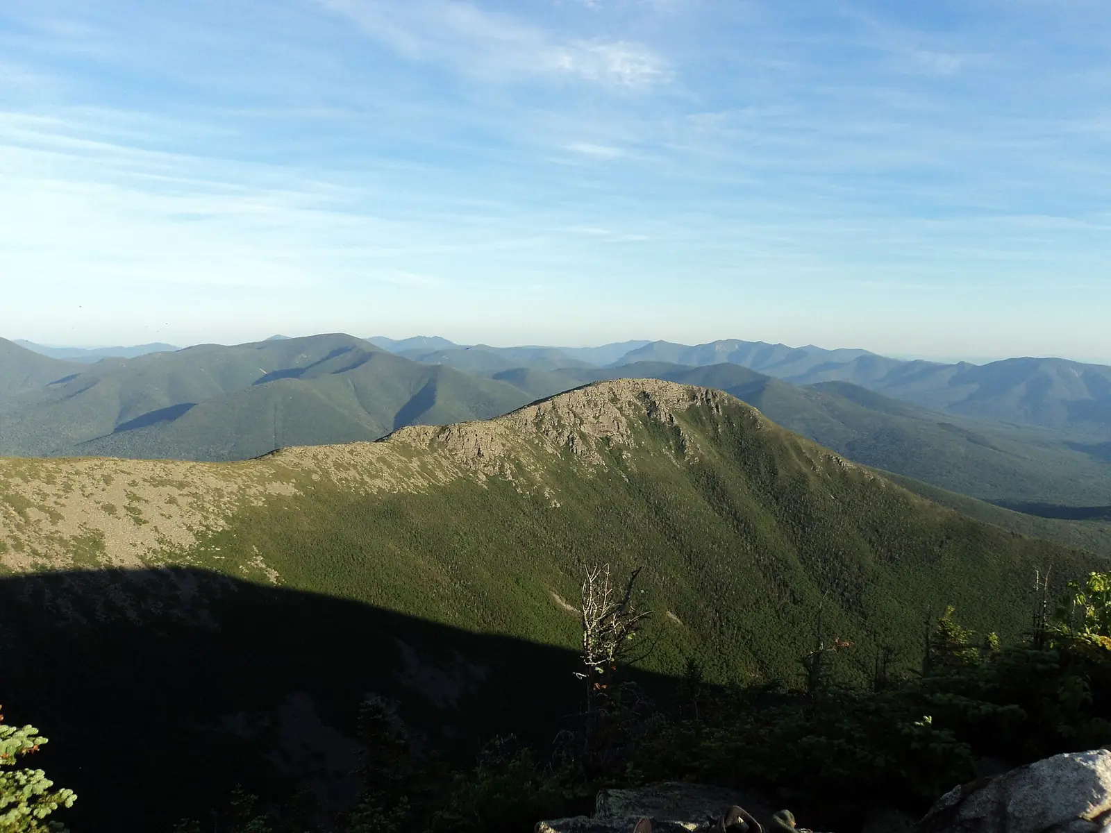 Bondcliff seen at sunset from West Bond in the Pemigewasset Wilderness, a bare rocky ridge falling away above dark spruce forest with layered New Hampshire ranges behind