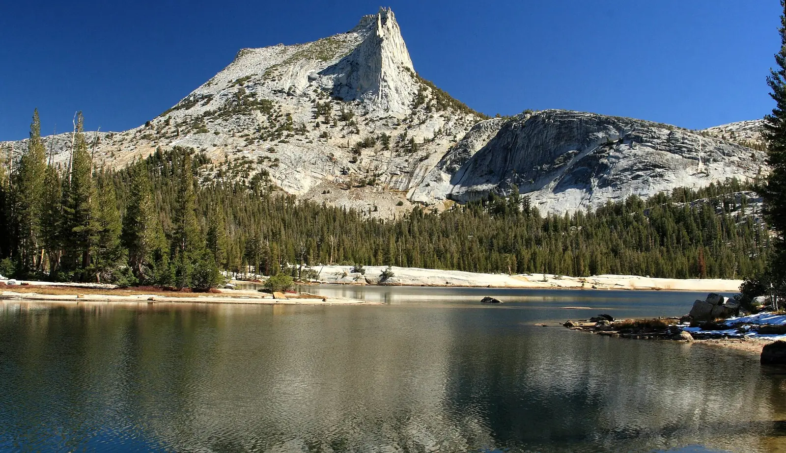 Cathedral Peak reflected in Cathedral Lake in Yosemite, a granite spire above pines with pale slabs running down to the water