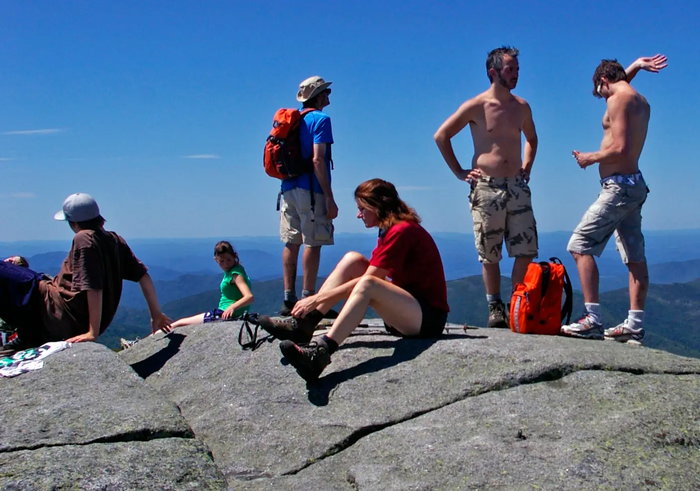 Hikers resting, standing and talking on the wide bare rock of the Algonquin Peak summit on a clear summer day