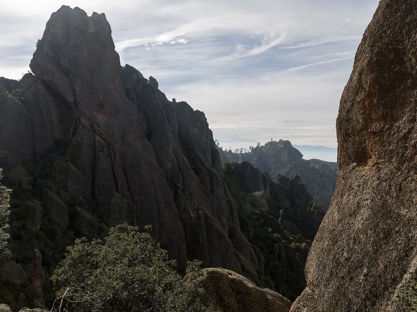 Steep volcanic rock spires and pinnacles rising above chaparral and dark green trees in the High Peaks of Pinnacles National Park