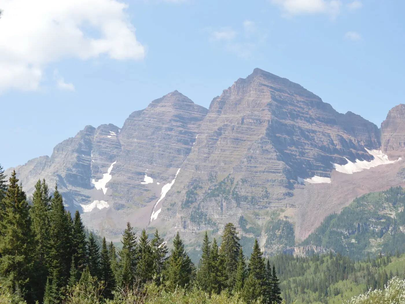 The two striped summits of the Maroon Bells seen from Crater Lake, with a belt of dark conifers filling the frame below the bare rock