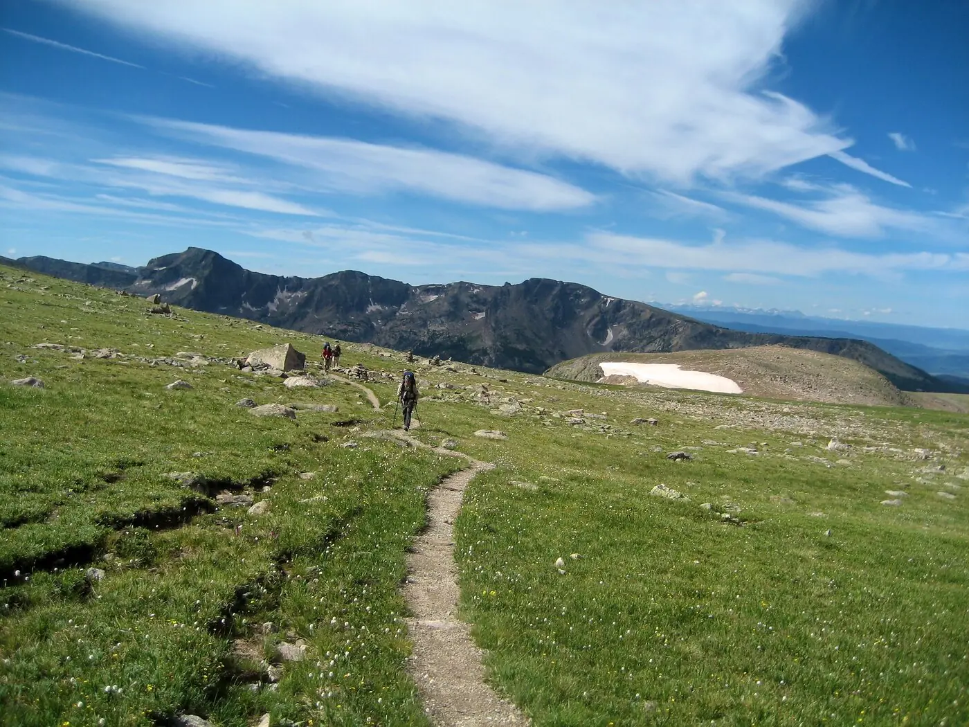 Hikers strung out along a narrow dirt path across open alpine tundra on Flattop Mountain, bare rocky peaks behind and no trees anywhere in the frame