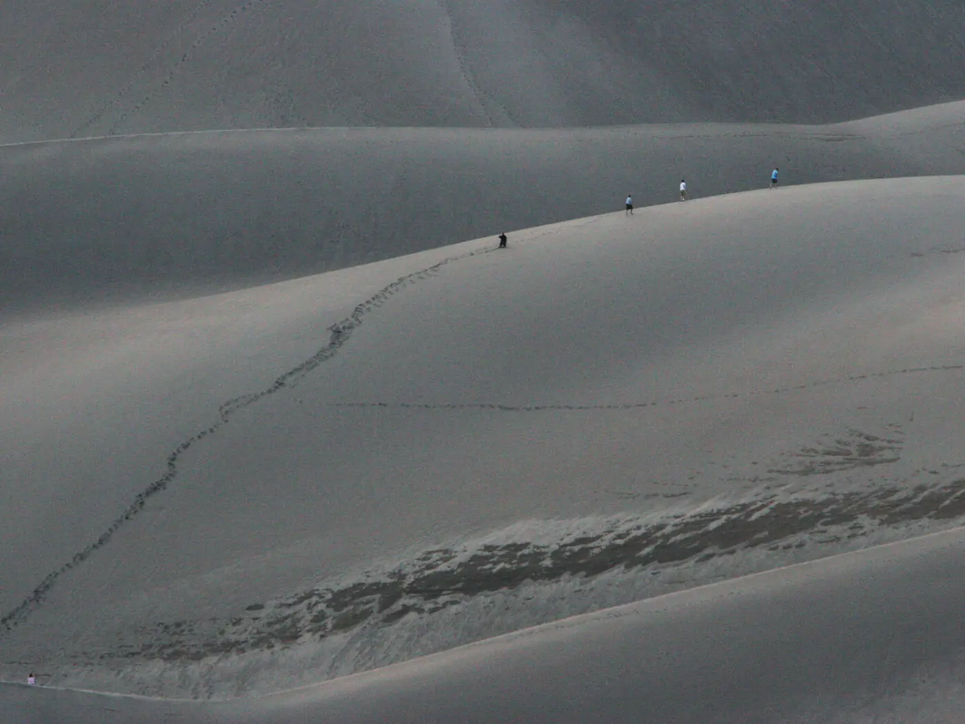 Four tiny figures strung out along the crest of a huge pale sand dune at Great Sand Dunes, a single line of footprints running up the ridge behind them