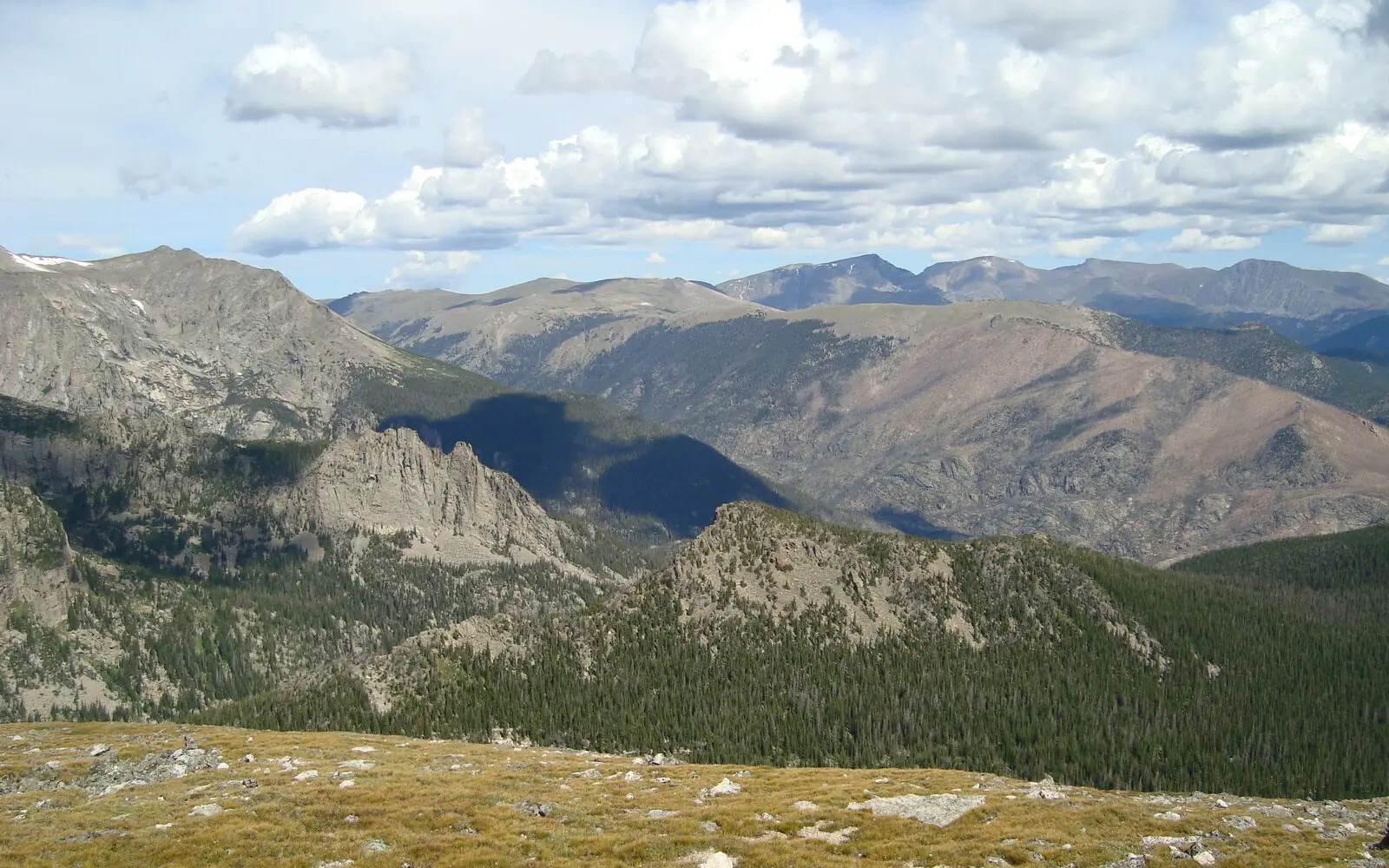 Open alpine tundra on the Flattop Mountain trail in Rocky Mountain National Park, looking north over forested valleys to bare peaks with cumulus building above them