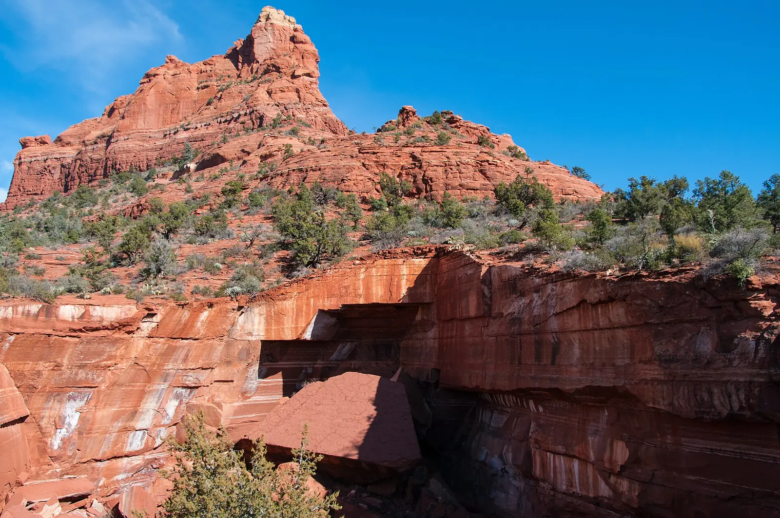 The Devil's Kitchen sinkhole on the Soldier Pass Trail in Sedona, a deep collapsed hollow in banded red sandstone with fallen slabs at the bottom and a red butte rising behind