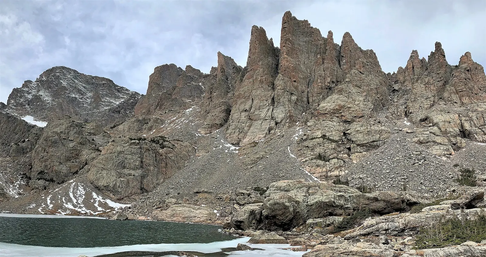 The jagged Cathedral Spires rising directly above Sky Pond, with ice still covering part of the water and snow in the gullies