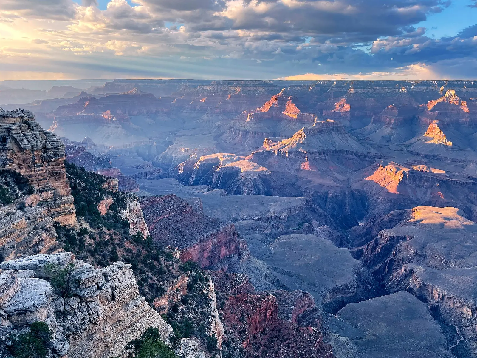 Evening light picking out the tops of the buttes at Mather Point on the South Rim, with a pale limestone ledge in the foreground and broken cloud overhead