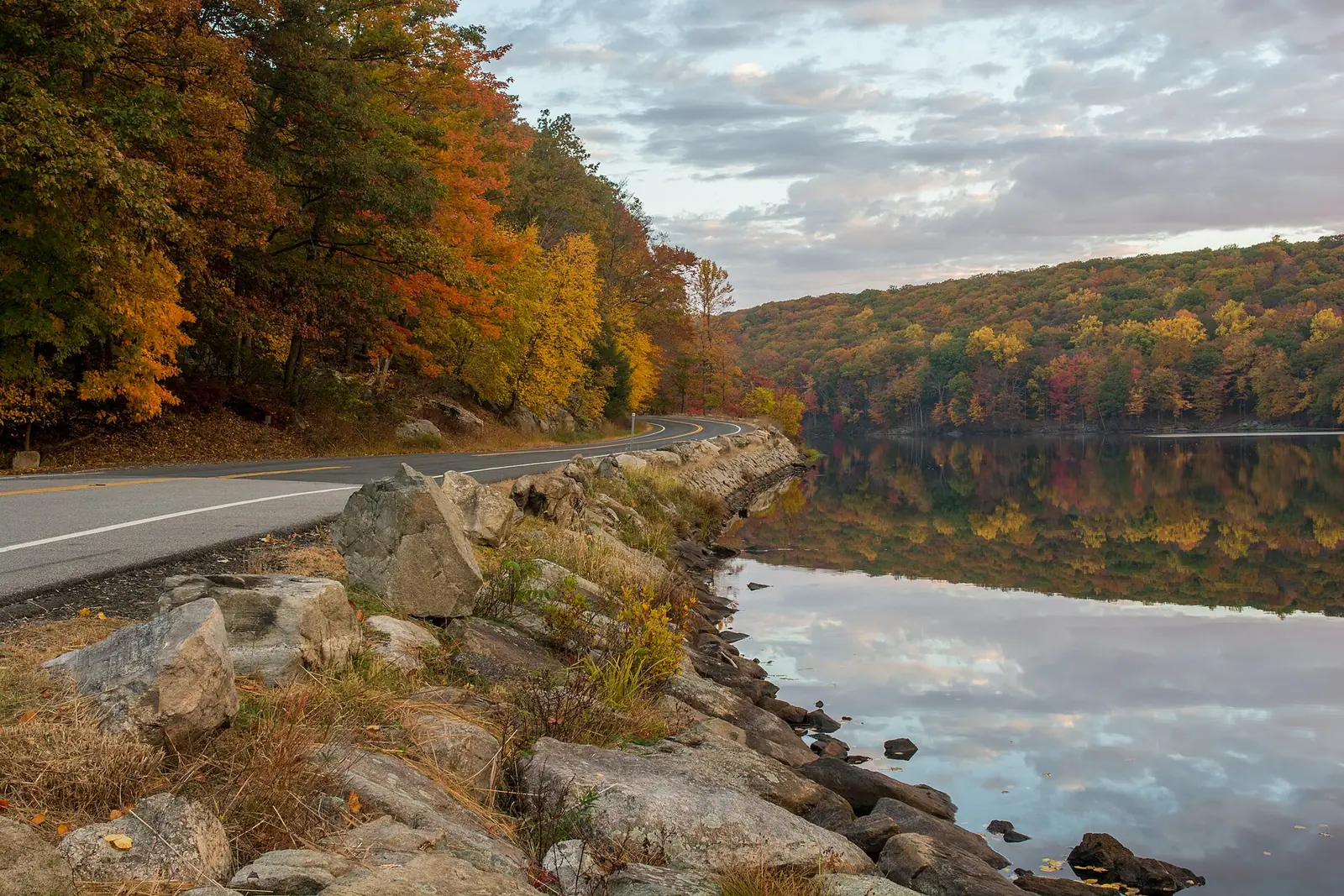 Seven Lakes Drive curving along the shore of Lake Askoti in Harriman State Park, the far bank in full orange and gold autumn color and mirrored in still water