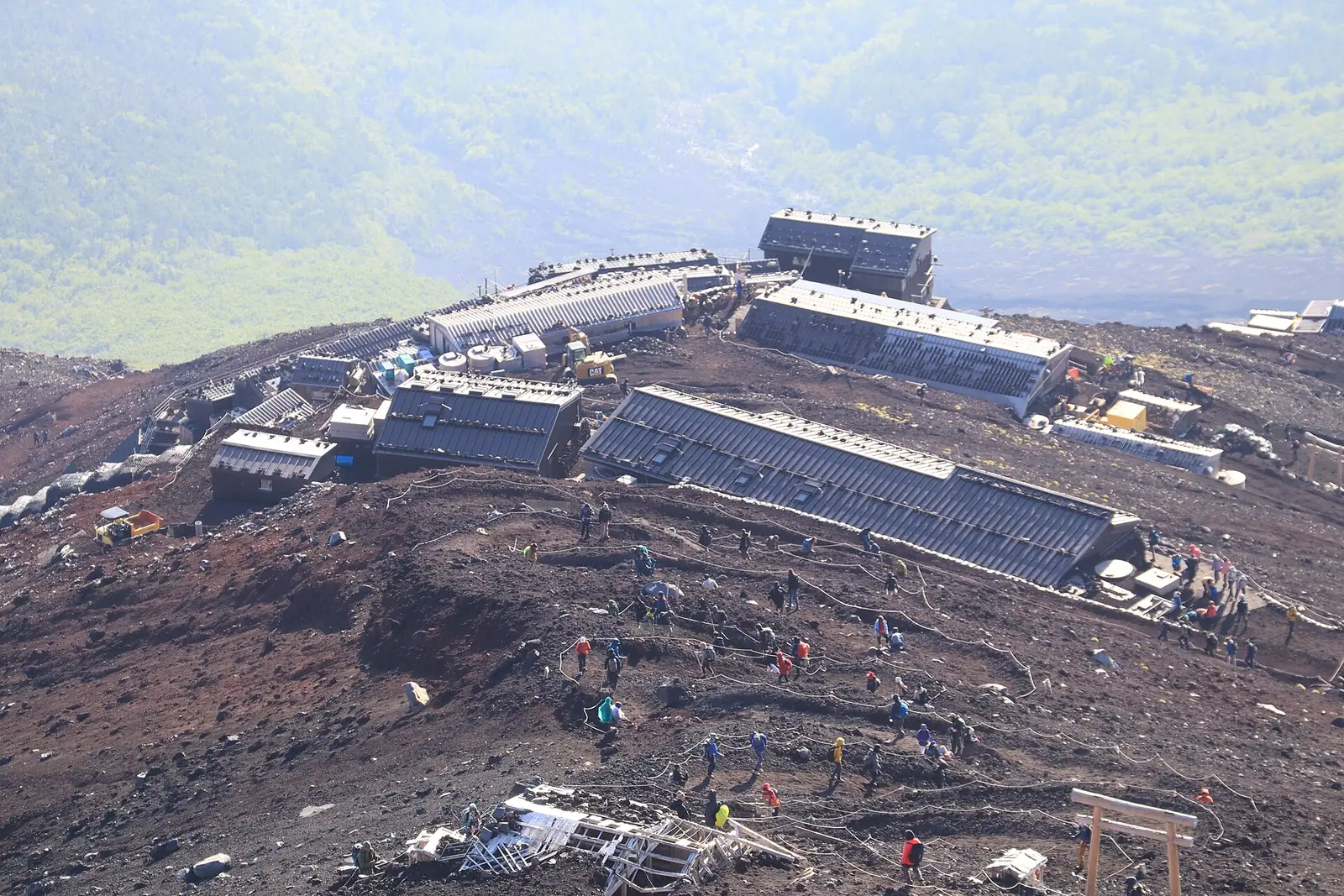 Mountain huts strung along the volcanic cinder slope of Mount Fuji's Yoshida Trail, with dozens of climbers spread out along the roped switchbacks below them