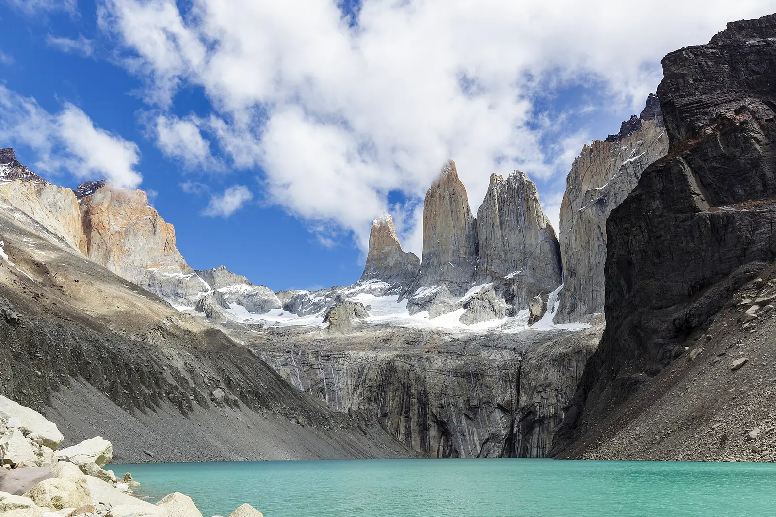 The three granite towers of Torres del Paine rising above a turquoise glacial lake, with snow on the ledges below them and blue sky above