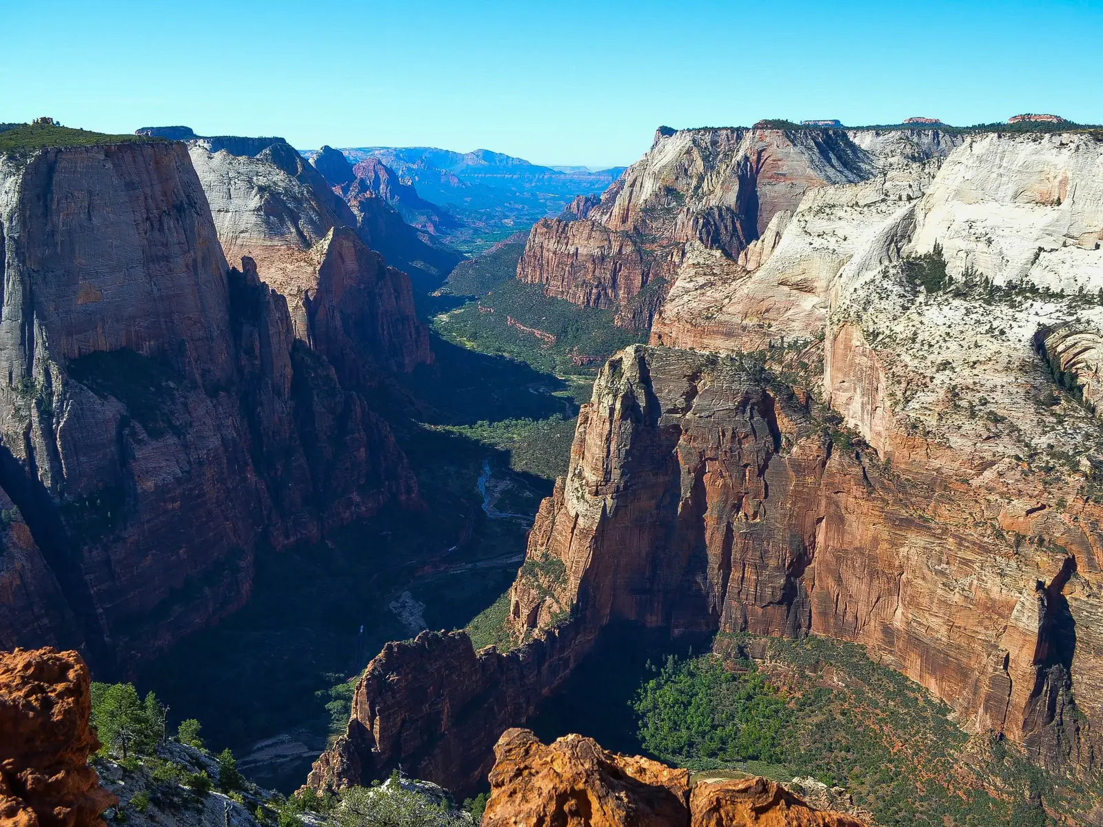The view south down Zion Canyon from Observation Point, with the fin of Angels Landing below and to the left, red and white cliffs on both sides and the canyon floor in deep shadow