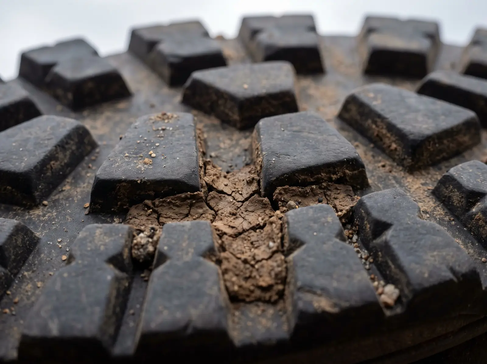 An extreme close-up of a hiking boot outsole showing tall square-shouldered rubber tread blocks with dried mud packed into the gaps between them.
